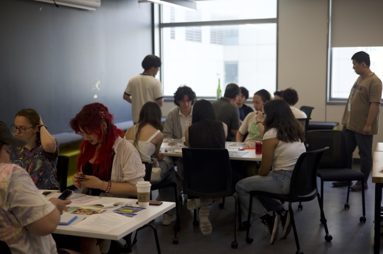 Tisch Summer High School Game Design students sit in small groups at tables working on game projects.